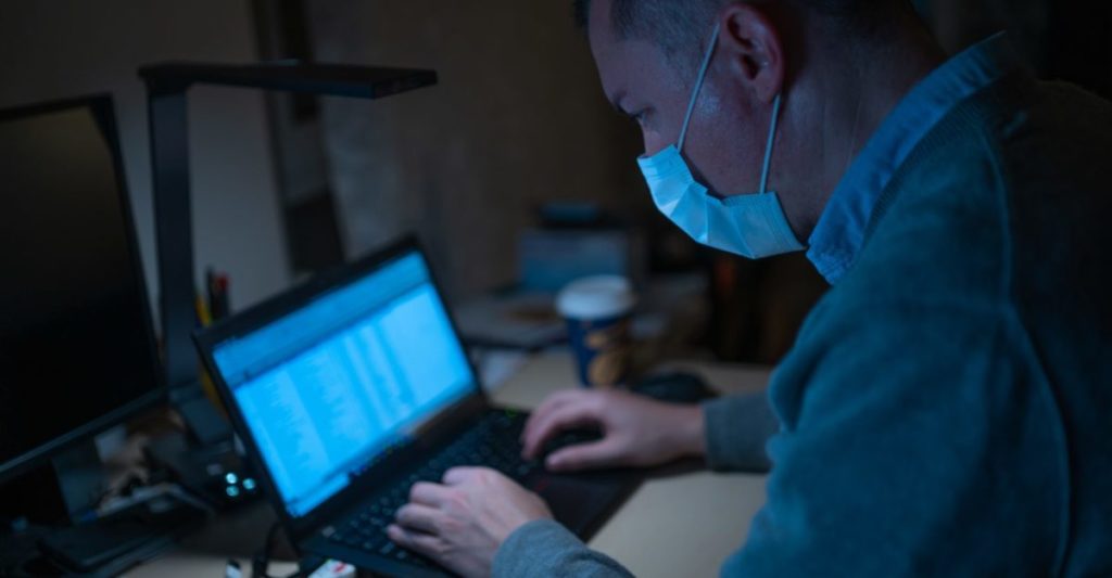 man is working on a laptop, wearing mask